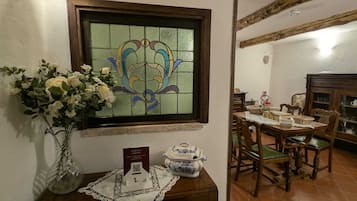 A dining area with a wooden table set for four, a vase of white flowers, and a stained glass window above.