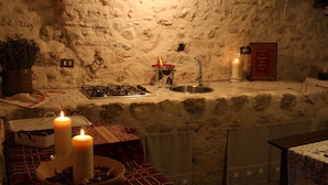 Une cuisine rustique avec un mur en pierre, une cuisinière à gaz, un évier et deux bougies allumées posées sur le comptoir.