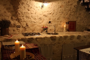Una cocina rústica con pared de piedra, una estufa a gas, un lavamanos y dos velas encendidas sobre la encimera.