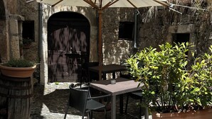 Une terrasse extérieure avec un sol en pierre, une table et des chaises, un grand parasol et des plantes en pot.