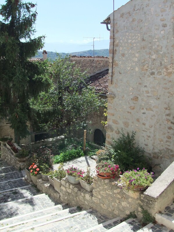 A stone staircase leading to a rustic building with a tiled roof, surrounded by lush greenery and potted flowers.