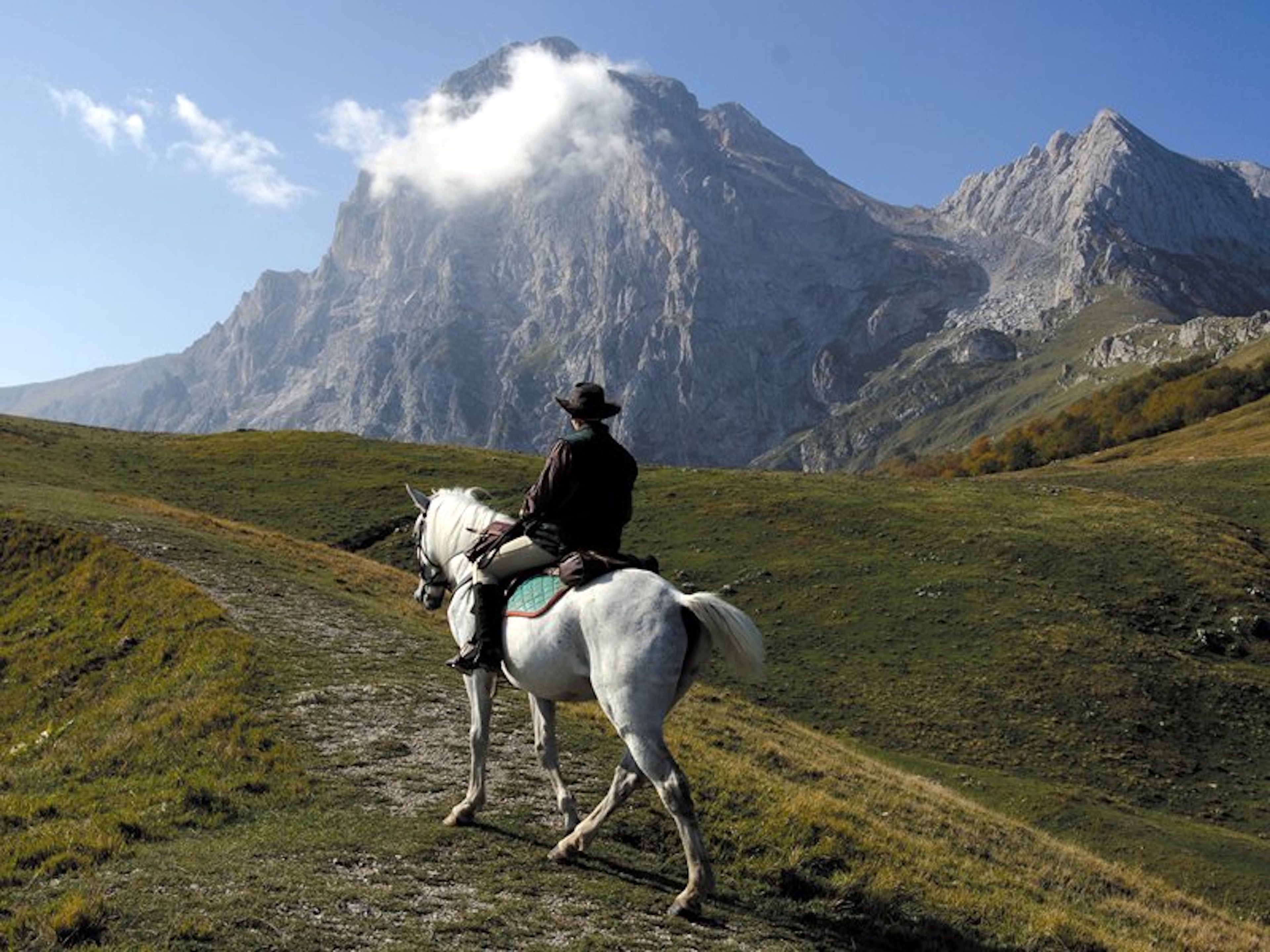 A person riding a horse on a dirt path with a mountainous backdrop.