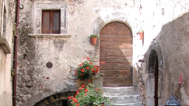 Un escalier étroit en pierre, surmonté d’une porte en bois, flanqué de murs en pierre et d’une rambarde en métal.