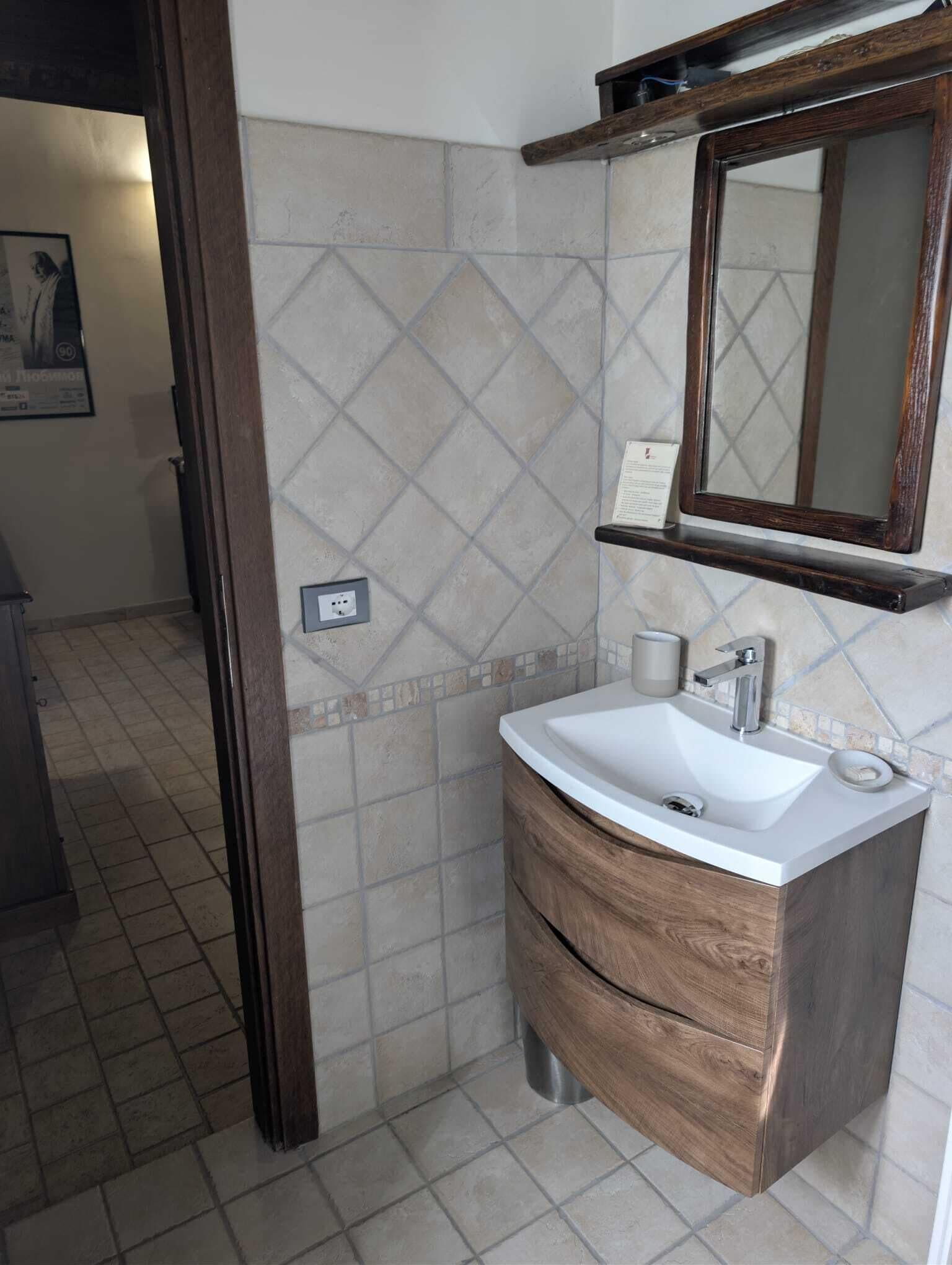 Un baño con tocador de madera, lavamanos blanco, espejo y pared con azulejos.