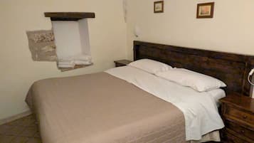 A single bed with a wooden headboard in a room with plain walls and tiled flooring.