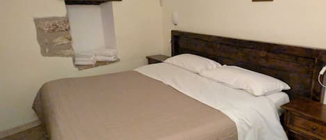 Una cama individual con cabecera de madera en una habitación con paredes lisas y suelo de baldosas.