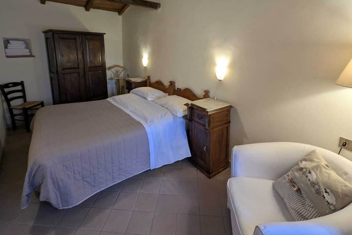 Ein Schlafzimmer mit Holzboden, einem Bett, einem Nachttisch, einem Stuhl und einem Schrank.