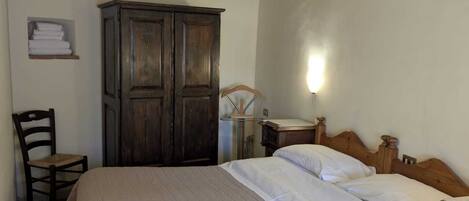 A bedroom with a wooden bed, a wooden wardrobe, a chair, and a bedside table.