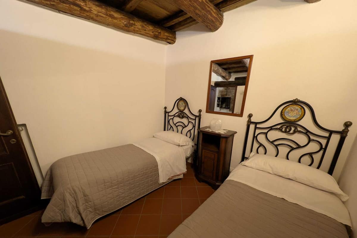 Ein kleines, gemütliches Schlafzimmer mit zwei Einzelbetten, einem Holzkopfteil, einem Nachttisch mit Lampe und einem Spiegel an der Wand.