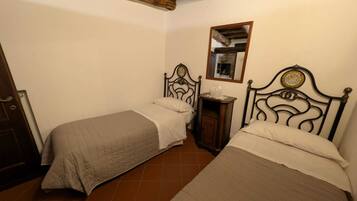 Un dormitorio pequeño y acogedor con dos camas individuales, cabecera de madera, mesita de noche con lámpara y espejo en la pared.