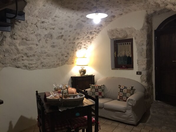 A cozy living room with a stone wall, a sofa, a table with a basket, and a lit lamp.