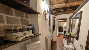 Un couloir étroit mène à une petite cuisine rustique équipée d’un poêle, de quelques étagères où sont rangées des serviettes et d’un radiateur.