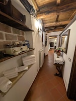Un pasillo estrecho con una zona de cocina rústica que incluye una estufa, estantes con toallas y un radiador.