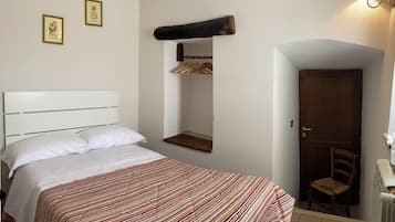 A bedroom with a bed, a wooden headboard, a wall-mounted shelf, a door, and a chair.