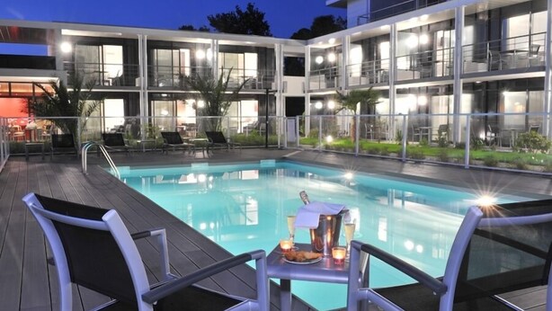 Un hotel moderno con piscina cubierta de vidrio, asientos al aire libre y una terraza bien iluminada.
