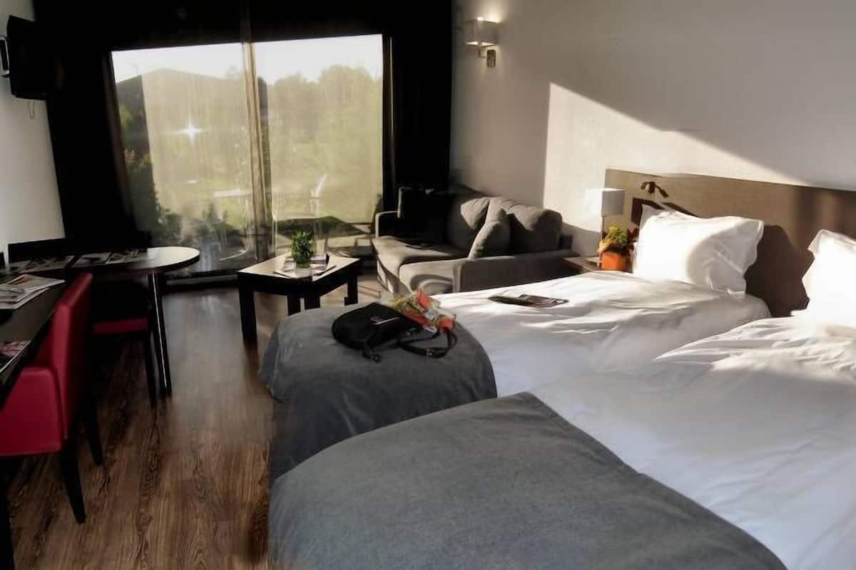 Een hotelkamer met een bed, een bureau, een stoel en uitzicht op het omliggende landschap.