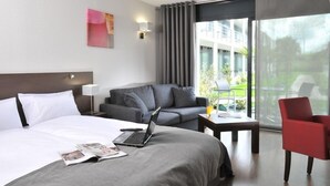 Una habitación de hotel moderna con una cama grande, un sofá gris, un sillón rojo y un ordenador portátil sobre la cama.