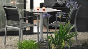 Una habitación de hotel moderna con un ventanal de vidrio que da a un balcón. La habitación tiene una cama con ropa de cama blanca, una mesita de noche con una lámpara y una pequeña mesa con velas.