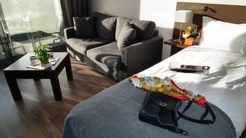 A hotel room with a bed, a sofa, a small table with a plant, and a nightstand with a lamp.