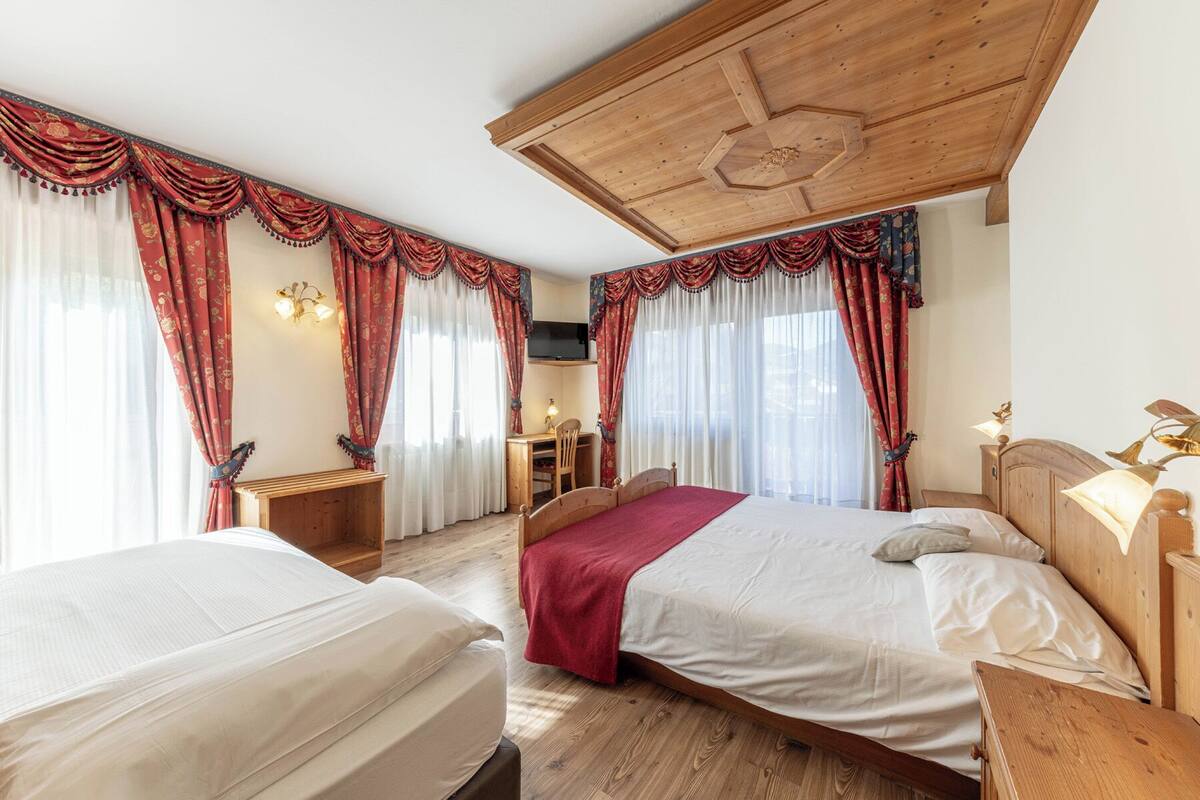 A hotel room with two beds, wooden headboards, a desk, and a television.