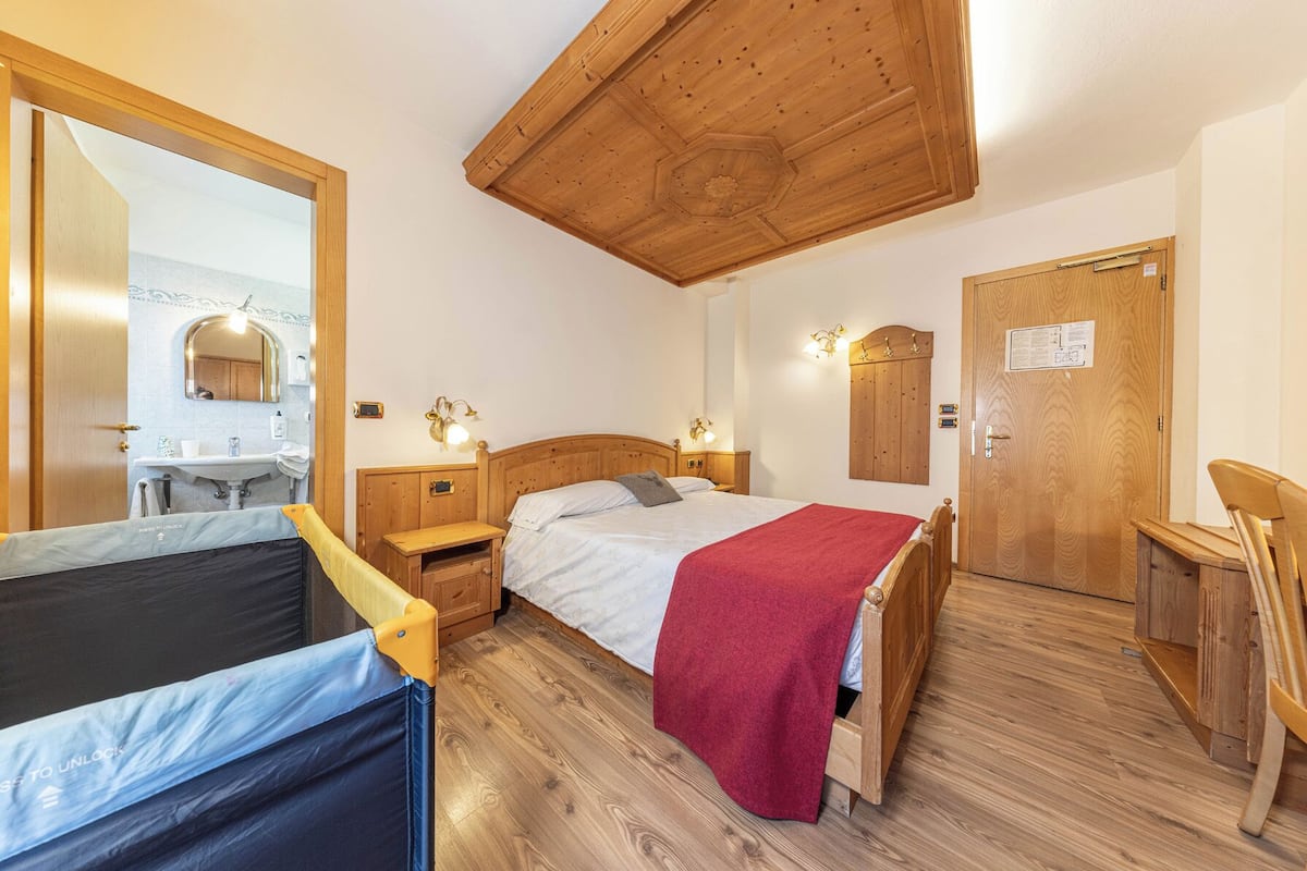 A bedroom with a wooden ceiling, a bed with a red blanket, a wooden nightstand, a wooden chair, and a wooden door.
