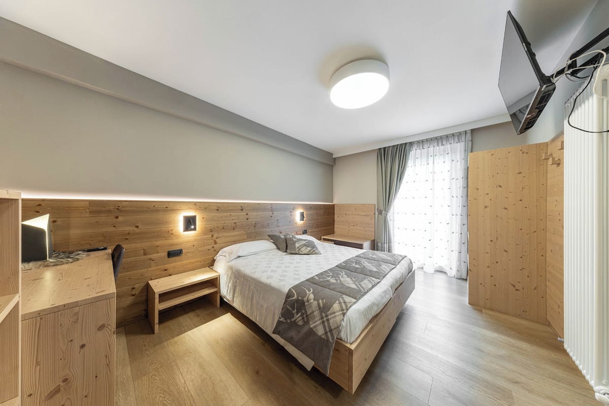 A modern bedroom with a wooden headboard, a bedside table, a bed with patterned bedding, and a ceiling light.