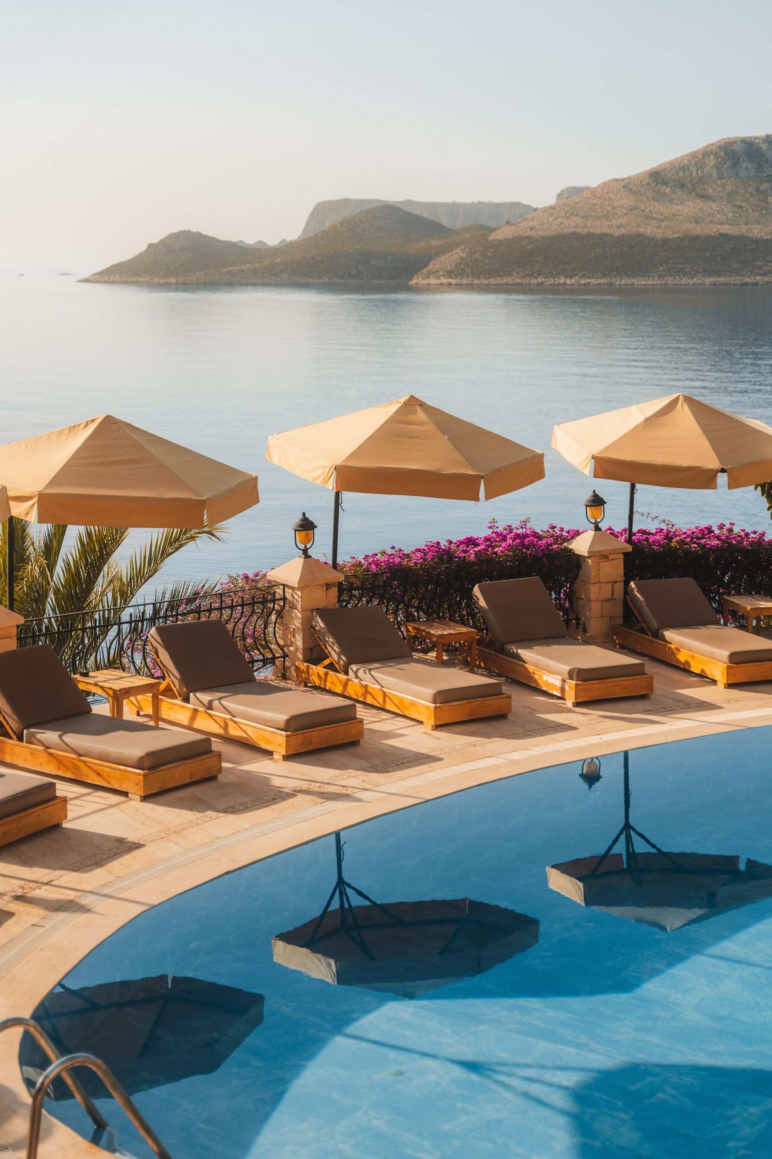 A poolside area with lounge chairs and umbrellas, overlooking a body of water and hills.