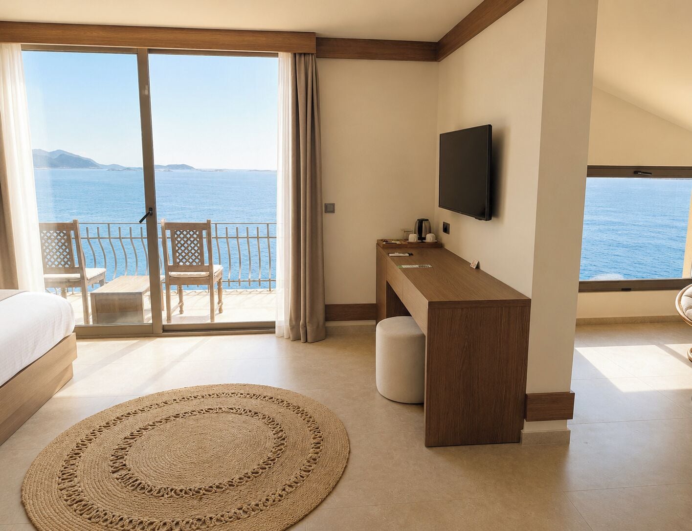 A hotel room with a bed, a desk, a television, and a view of the sea.