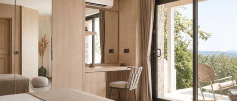 A bedroom with a large bed, a desk, and a view of a balcony with outdoor furniture.