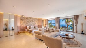 Una sala de estar moderna con una pared de piedra, ventanas amplias que dan al mar y una zona de estar acogedora.