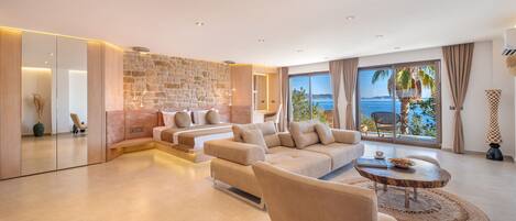 A modern living room with a stone wall, large windows with a view of the sea, and a cozy seating area.