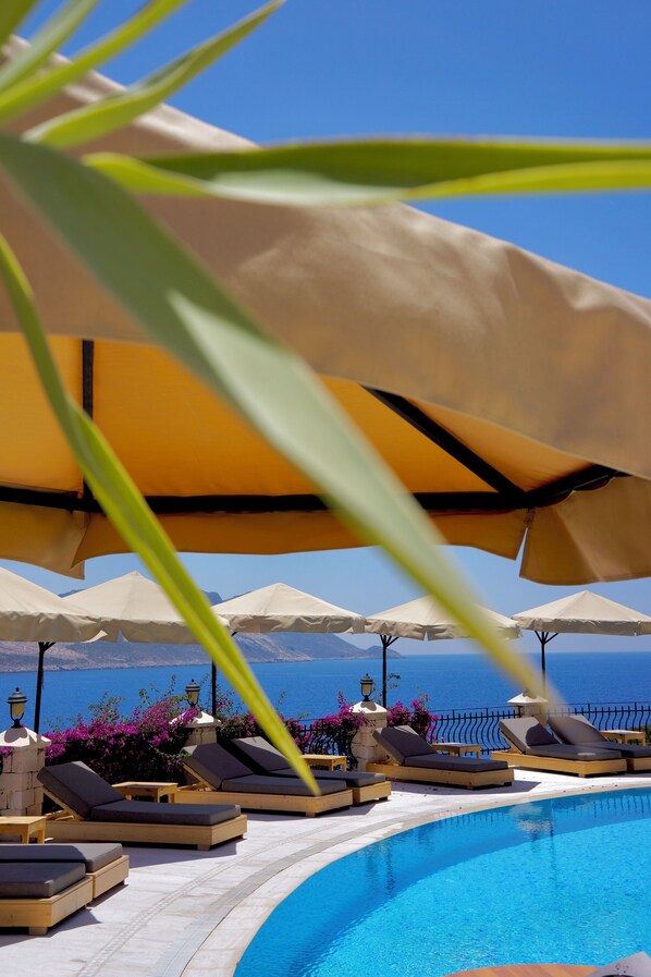 A poolside area with lounge chairs and umbrellas, a clear blue sky, and a view of the sea. - Villa Tamara Hotel (Kas)