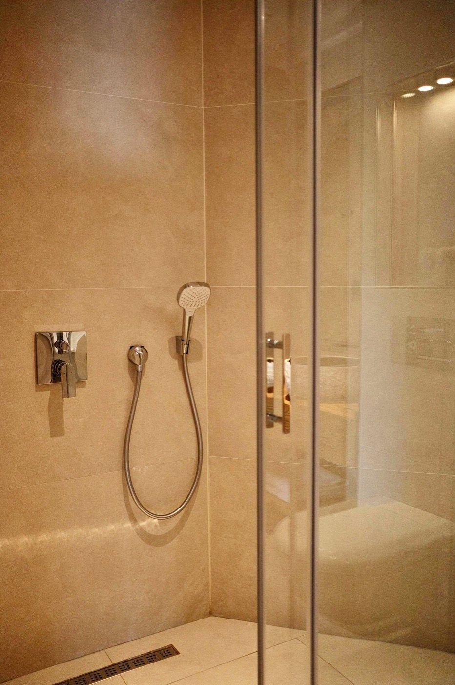 Une salle de bain moderne dotée d’une douche à parois de verre, d’un pommeau de douche à main et d’un robinet mural.