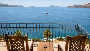 Un balcón con dos sillas de madera, una mesa y vista al mar con un velero.