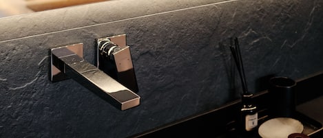 A modern bathroom with a stone countertop, a mirror, a towel rack, and a small bottle of soap.