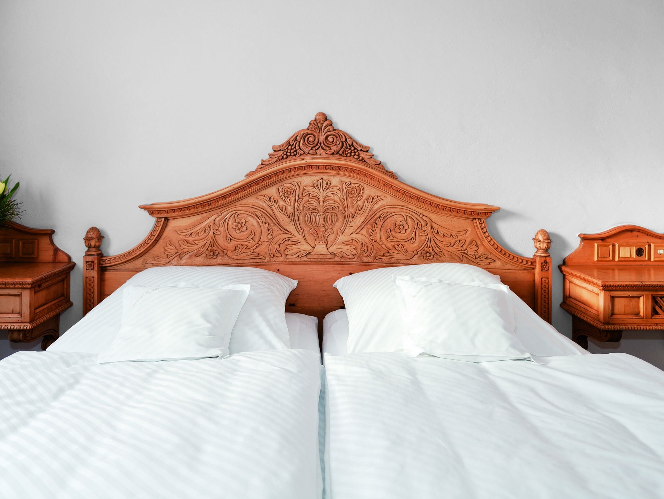 Un letto matrimoniale con una testiera in legno intagliata, due comodini e biancheria da letto bianca.