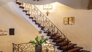 Eine prächtige Treppe mit aufwendigen Metallgeländern und sternförmigen Verzierungen, die zu einer Zwischenebene mit einem Blumentopf und einem kleinen Tisch führt.