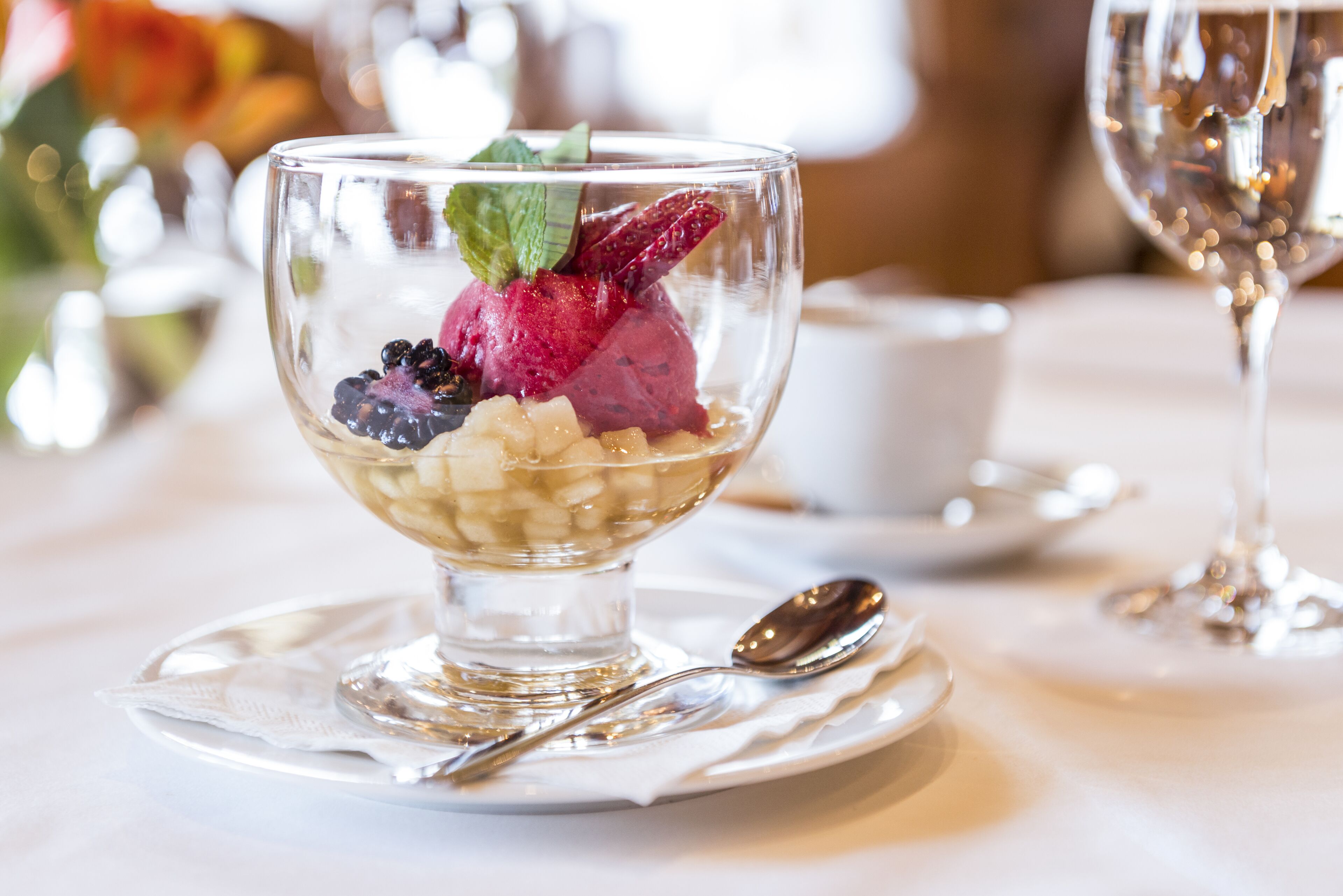 Postre en un bol de vidrio transparente sobre un plato blanco, con una cuchara a un lado.