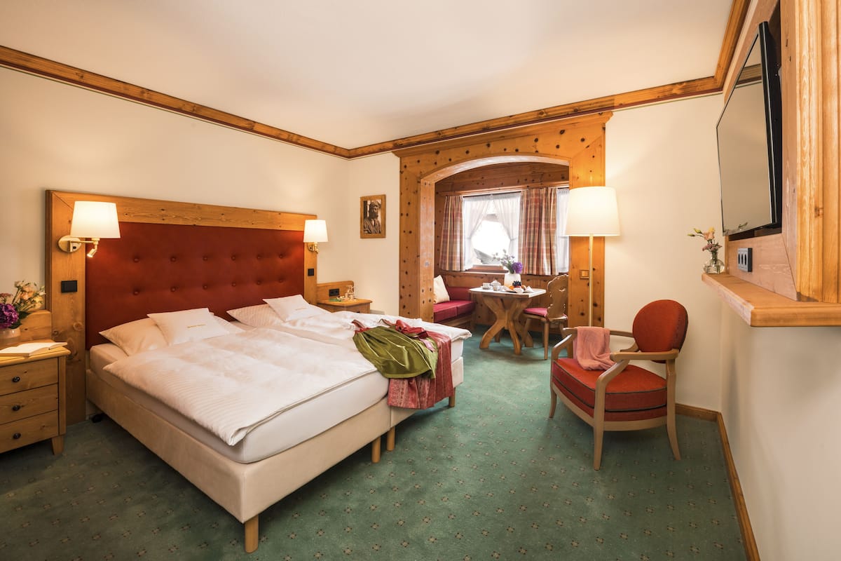 Ein Hotelzimmer mit einem großen Bett, einem Holzkopfende, einem kleinen Tisch mit Stuhl und einem fenster mit Vorhängen.