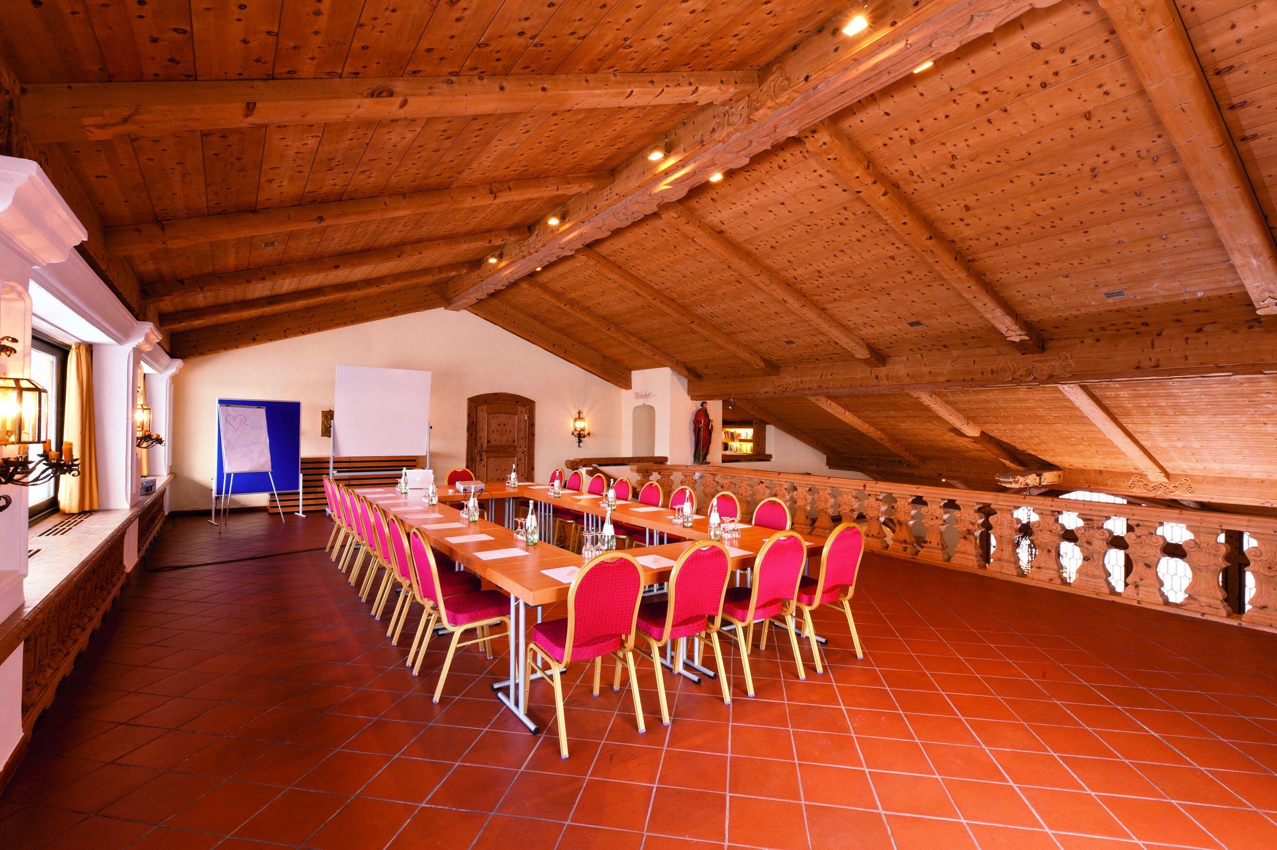 Un salón de conferencias con techo de madera alto, suelo de baldosas rojas y largas mesas con sillas rosadas.