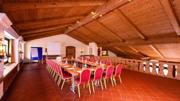 Un salón de conferencias con techo de madera alto, suelo de baldosas rojas y largas mesas con sillas rosadas.