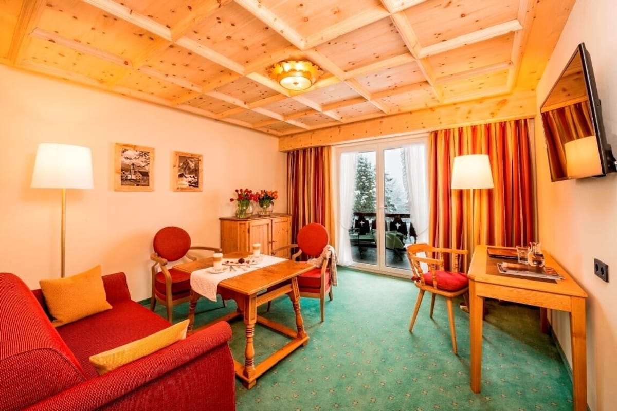 Ein gemütliches Zimmer mit Holzbalkendecke, einem Esstisch mit Stühlen, einer Couch und einem an der Wand befestigten Fernseher.