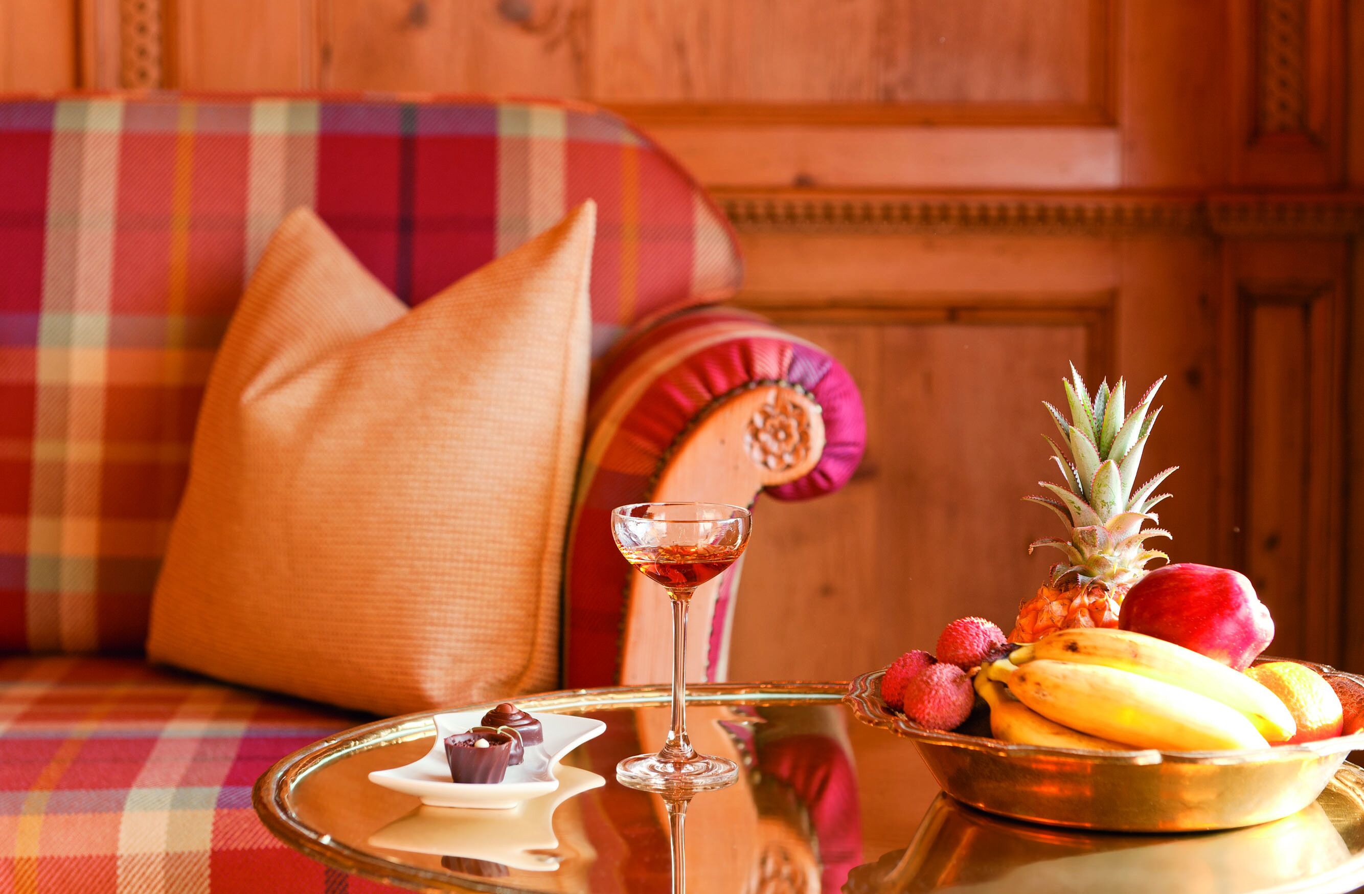 A cozy seating area with a plaid sofa, a glass table with a fruit bowl and a glass of red wine.