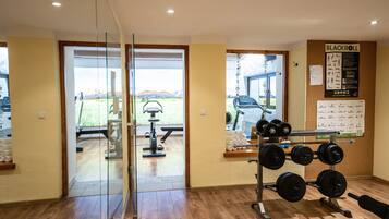 Un gimnasio con equipo de ejercicio, un soporte para pesas y vistas a un paisaje montañoso a través de puertas de vidrio.