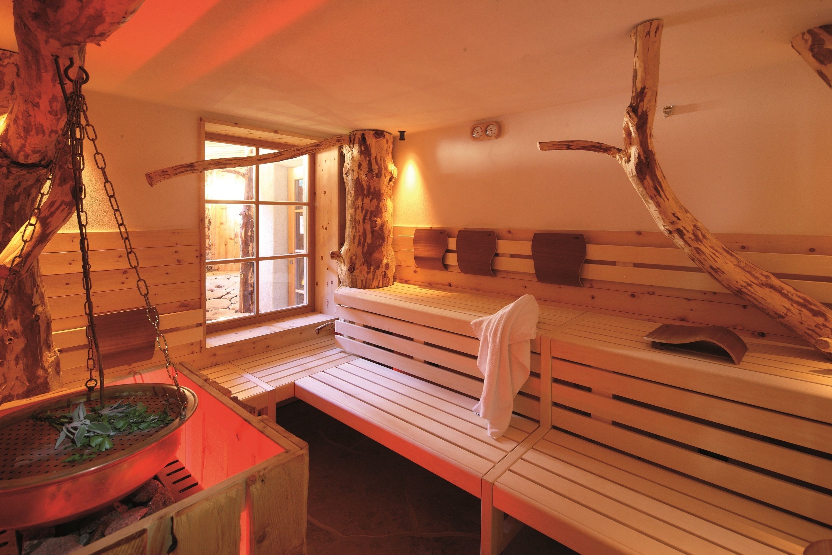 A sauna room with wooden benches, a hanging sauna, and a stone wall.