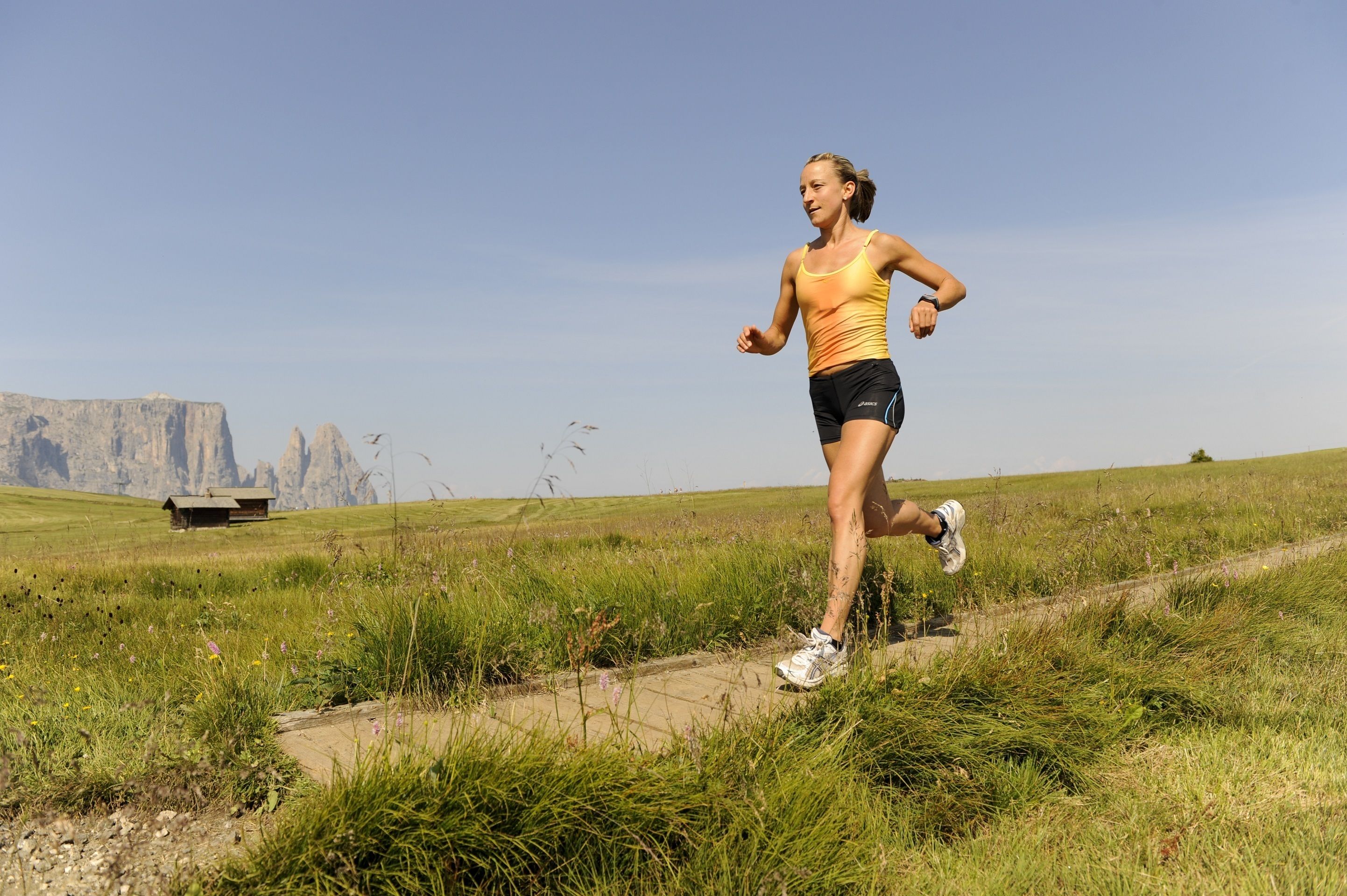 A person running on a grassy path with a clear sky and distant rock formations.