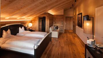 Un dormitorio con techo de madera, una cama con ropa blanca, una mesita de noche con lámpara y una pequeña zona de estar con una silla y una mesa.