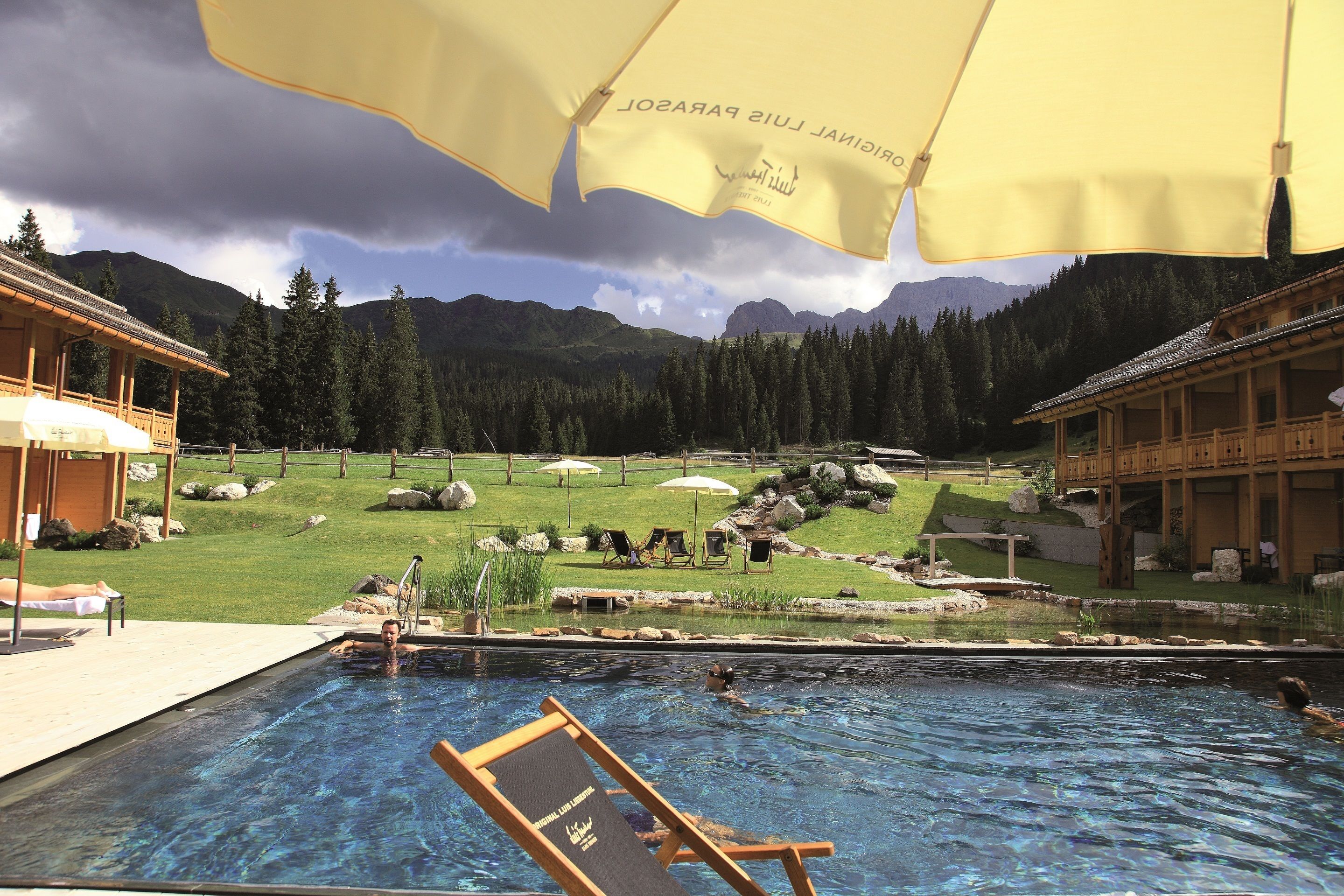 Ein Swimmingpool mit Liegestühlen, ein Holzgebäude und eine Berglandschaft im Hintergrund.