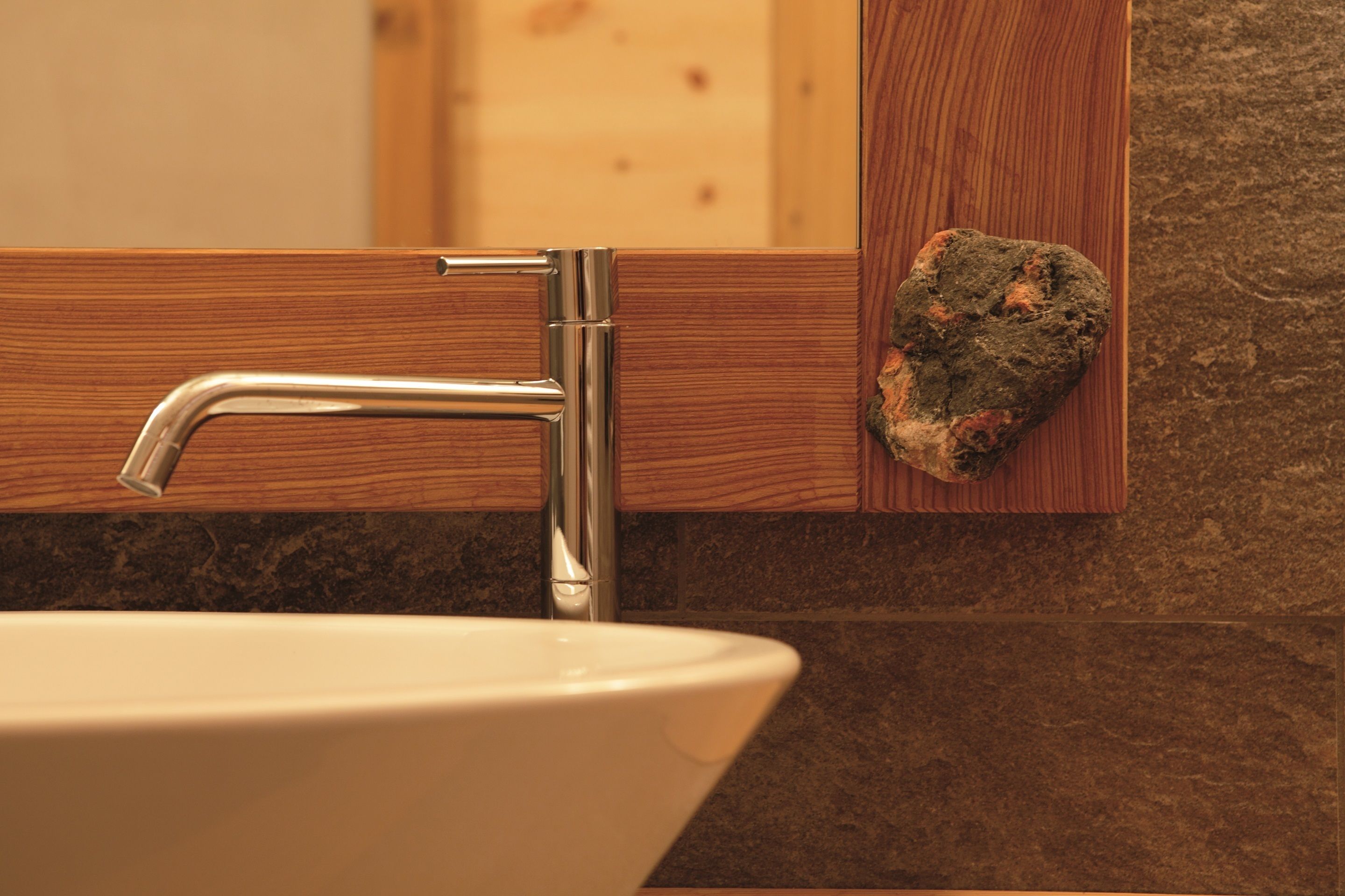 A bathroom with a white sink, a chrome faucet, wooden cabinetry, and a stone wall.