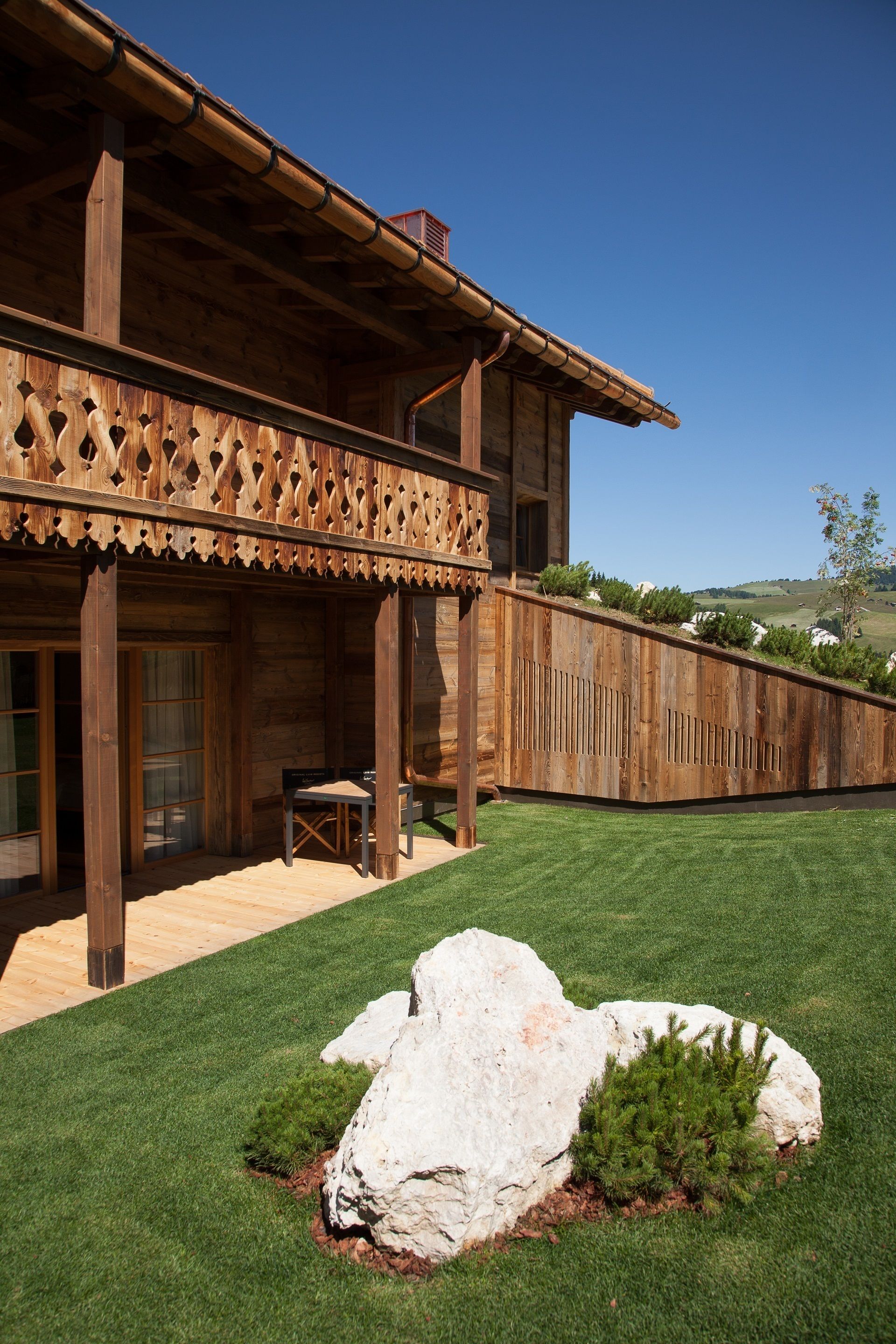 A wooden building with a balcony, a lawn, and a large rock.